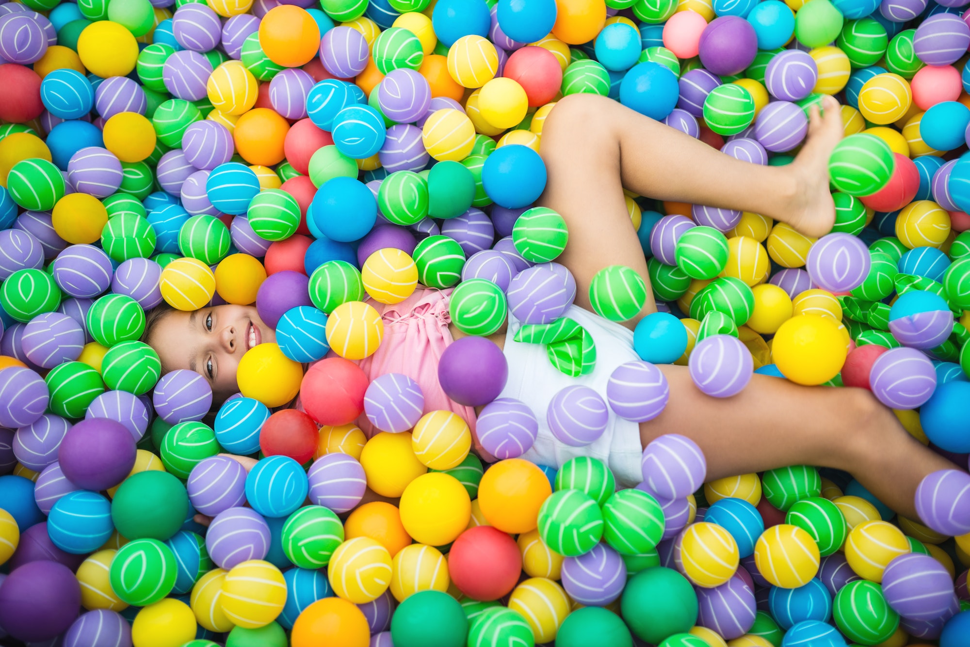 Child lying in pool with plastic balls